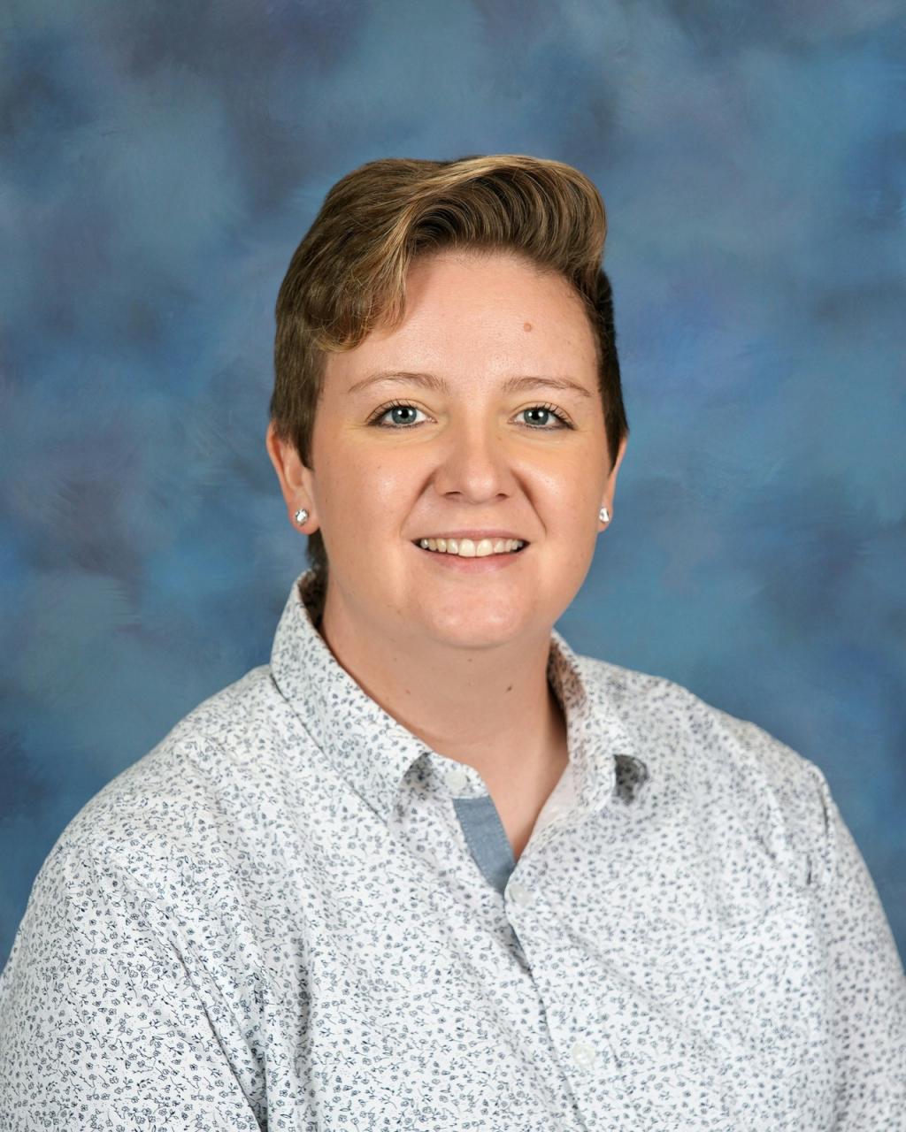Lady with short brown hair, wearing a flowered shirt and earrings